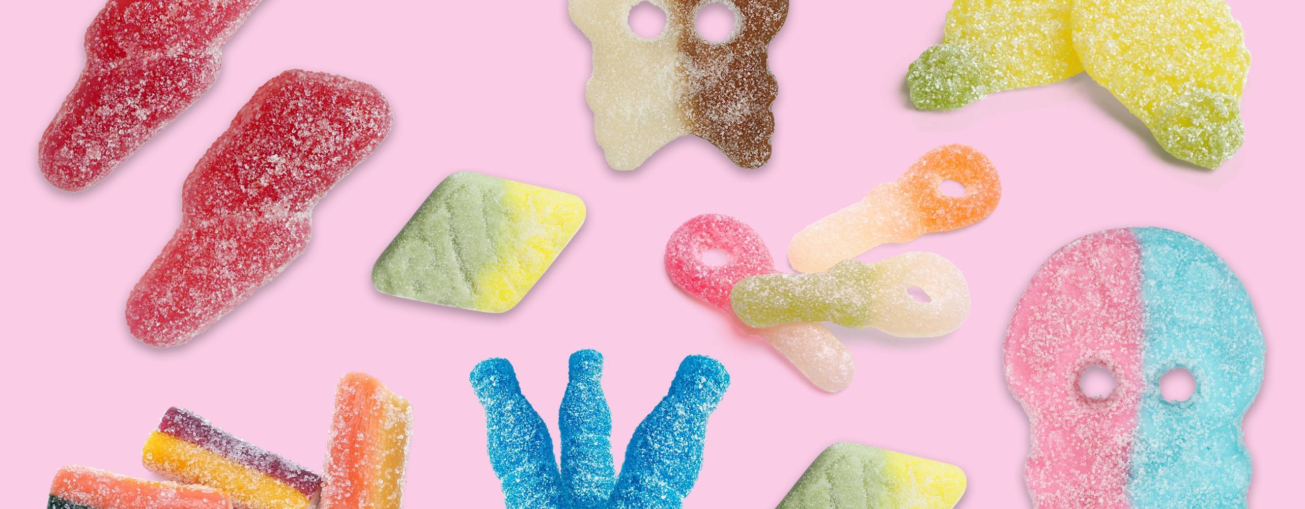 flera sura veganska godisar utspridda mot en ljusrosa bakgrund