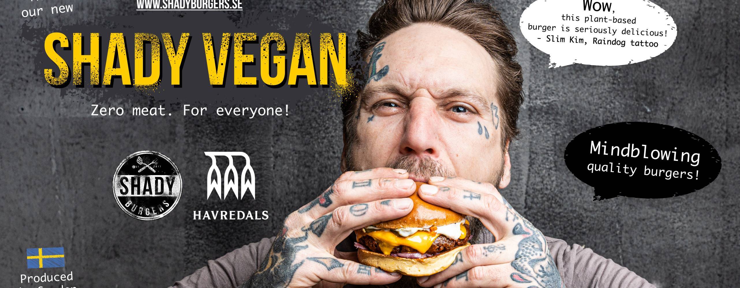 Tatuerad man som äter en vegansk hamburgare mot en mörk bakgrund