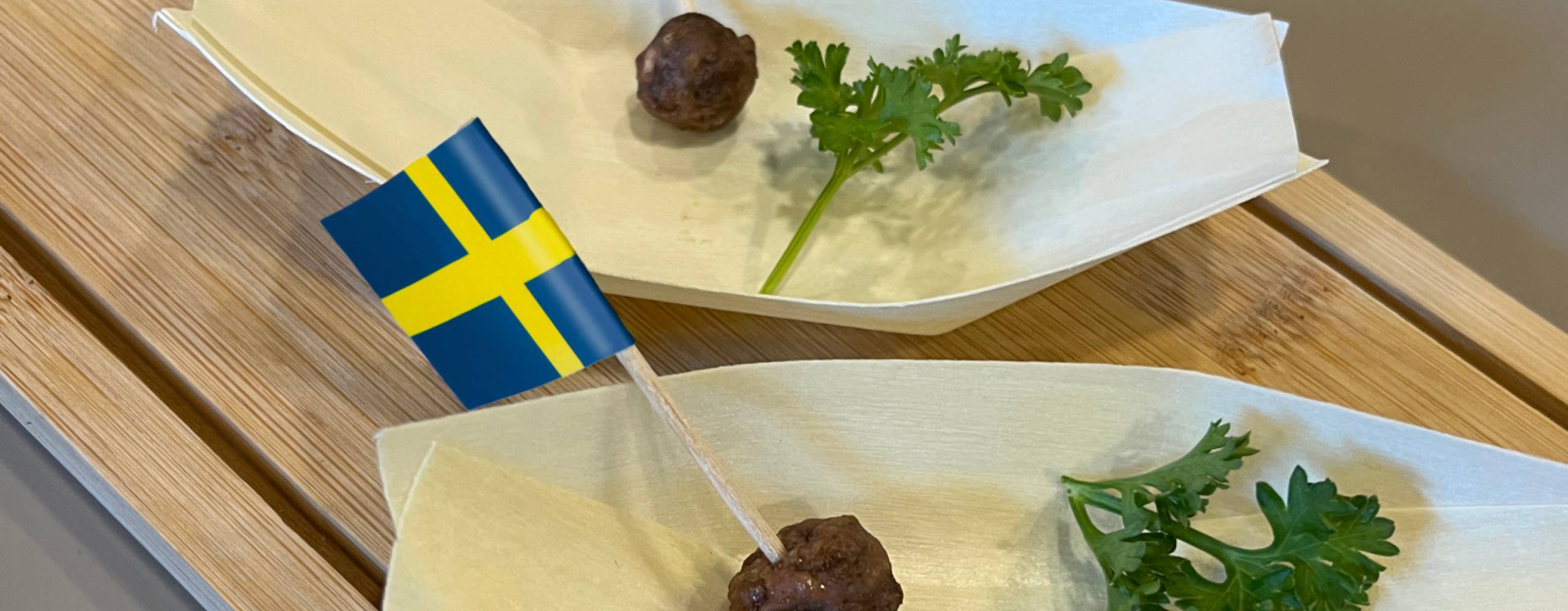 Två odlade köttbullar på vita fat med små svenska flaggor i och kvistar med persilja på sidan om