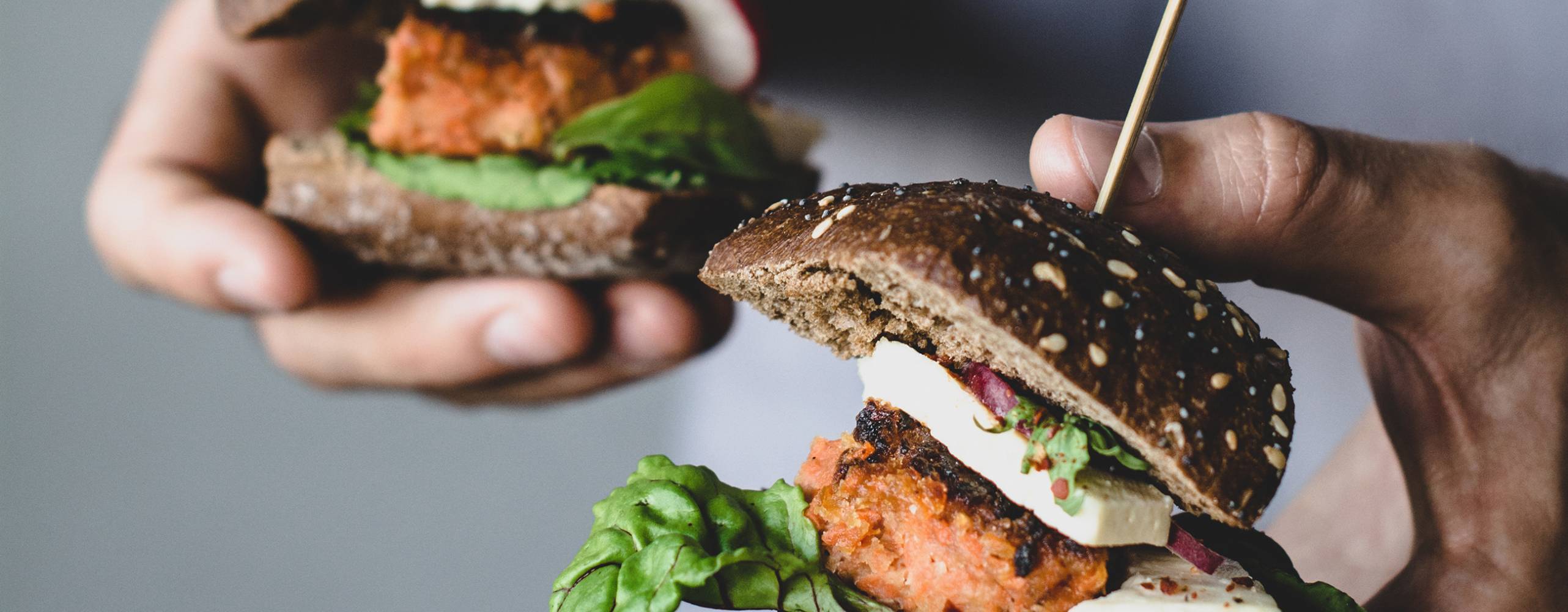 Ung man som håller två växtbaserade morotstofuburgare. Närbildvy, selektivt fokus