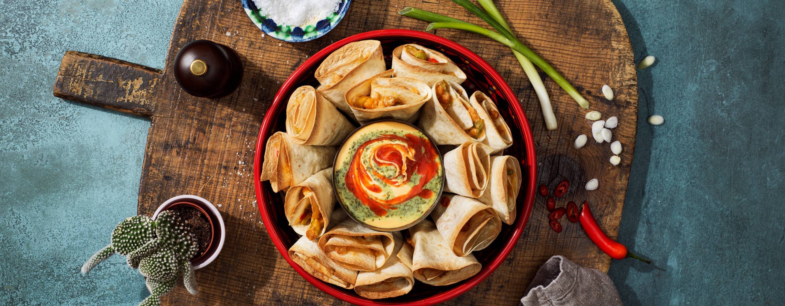 En tallrik med nachos på en skärbräda i trä som står på ett bråblåt bord