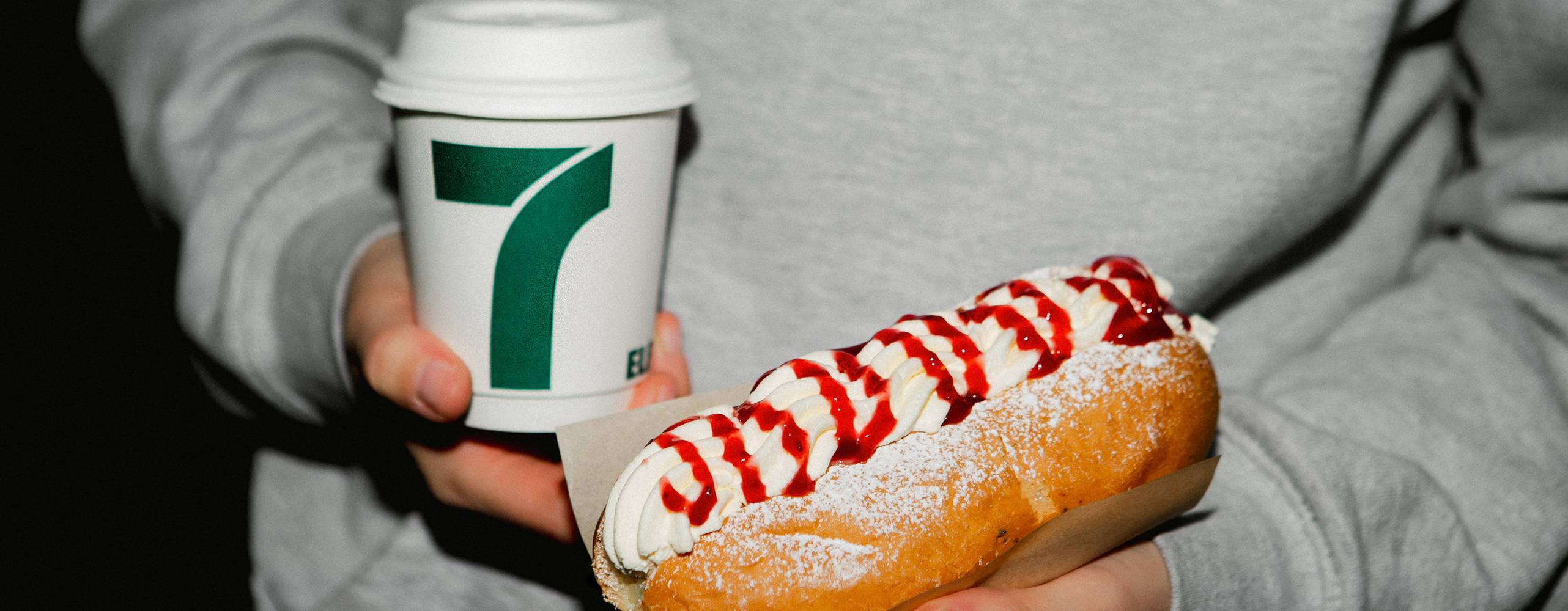 Man som håller en pappmugg med kaffe i andra handen och en semmelbakelse i korvbröd i den andra