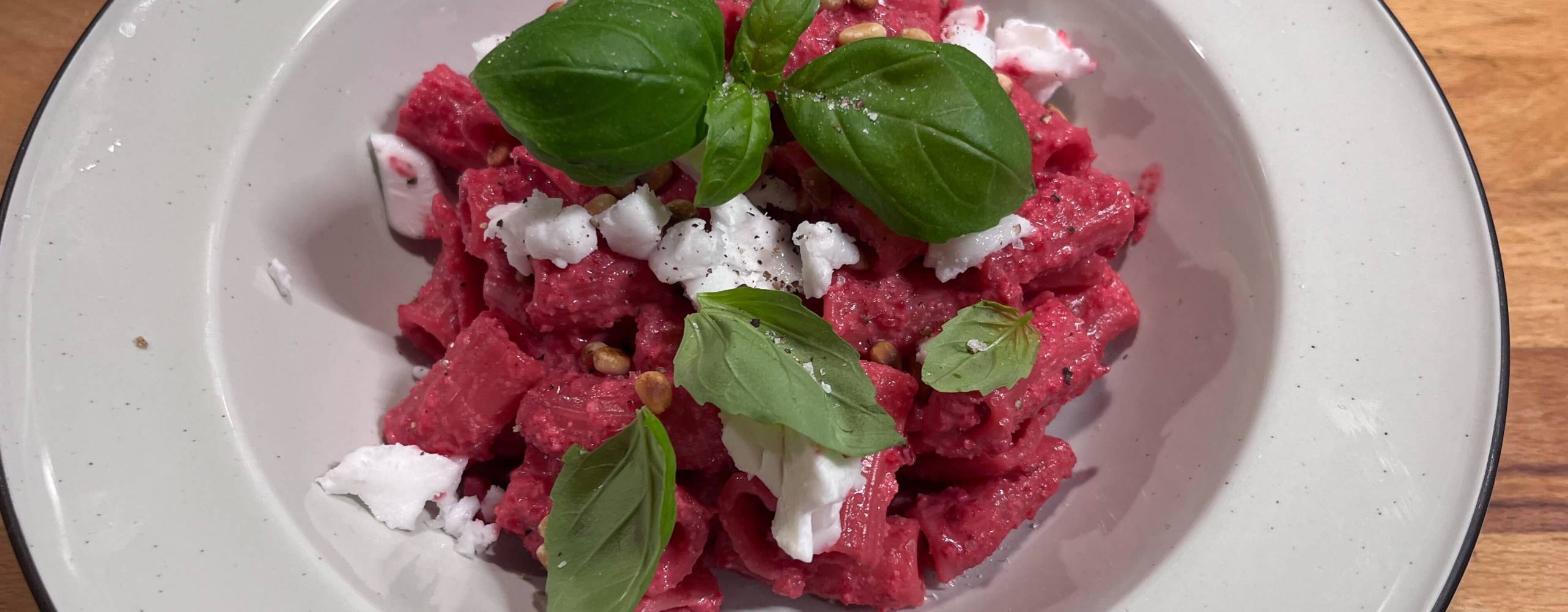 En djuptallrik med rödbetspasta, dekorerad med vegansk feta, pinjenötter och basilika