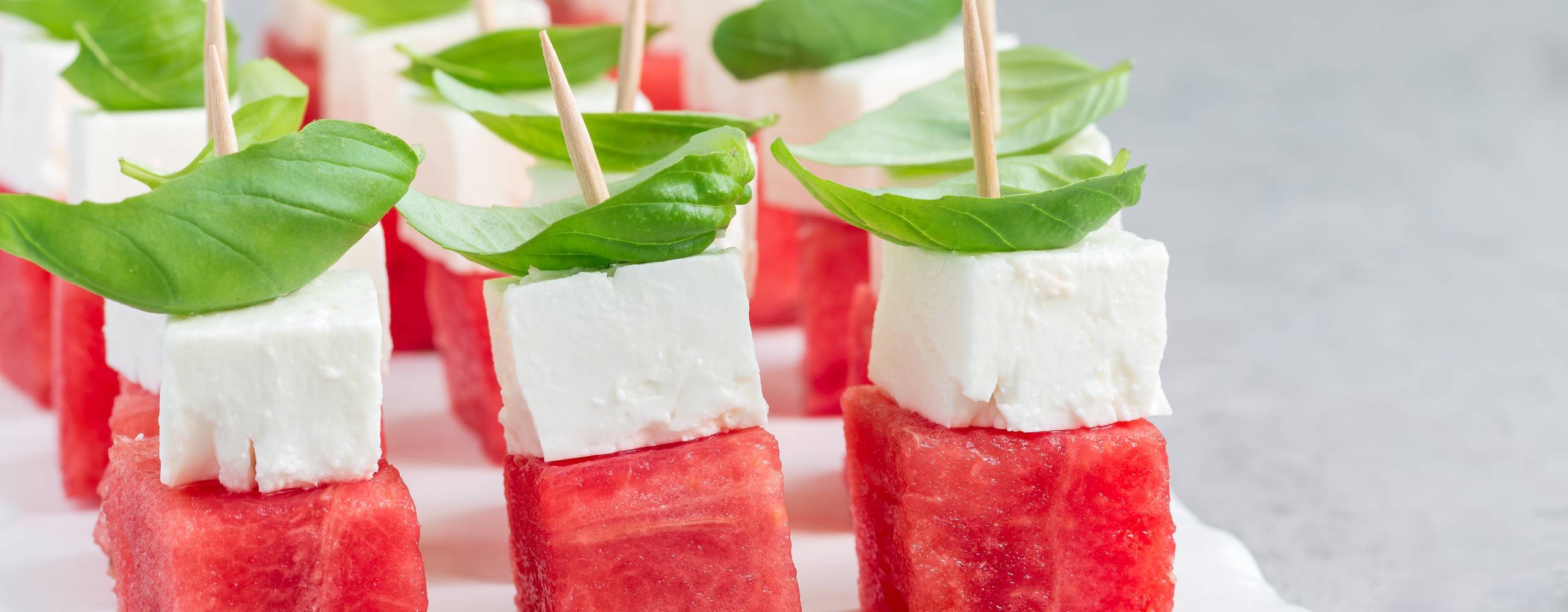 Snittar med melon, vegansk fetaost och basilika på ett vitt fat.