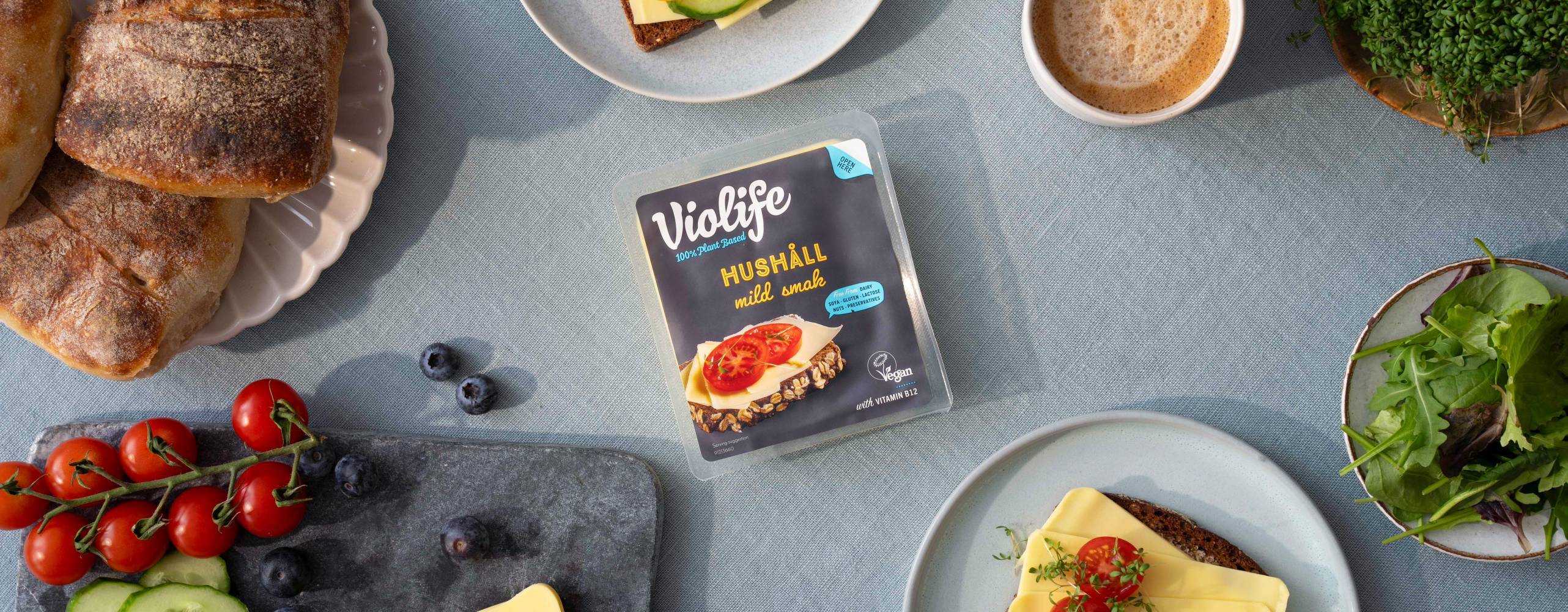 ett frukostbord med bröd, tomater, gurka, grönt och växtbaserad ost