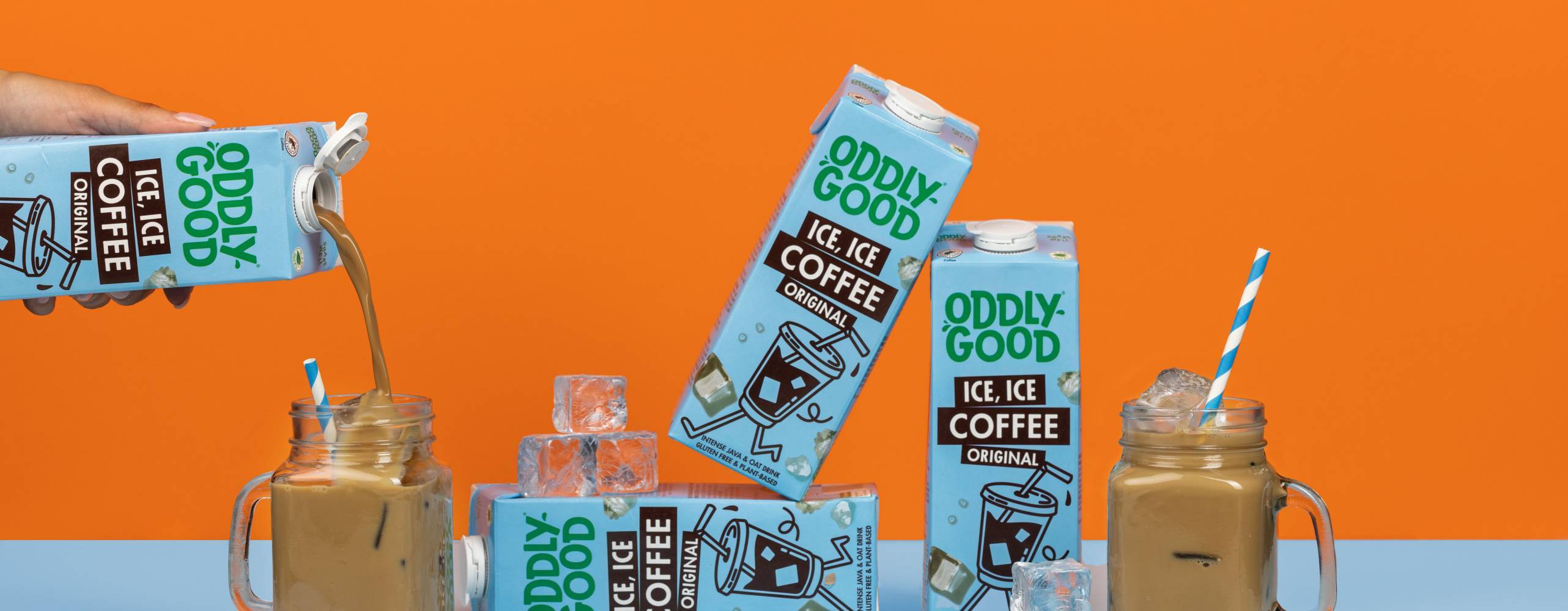 Förpackningar med växtdryck och glas med iskaffe mot en orange bakgrund.