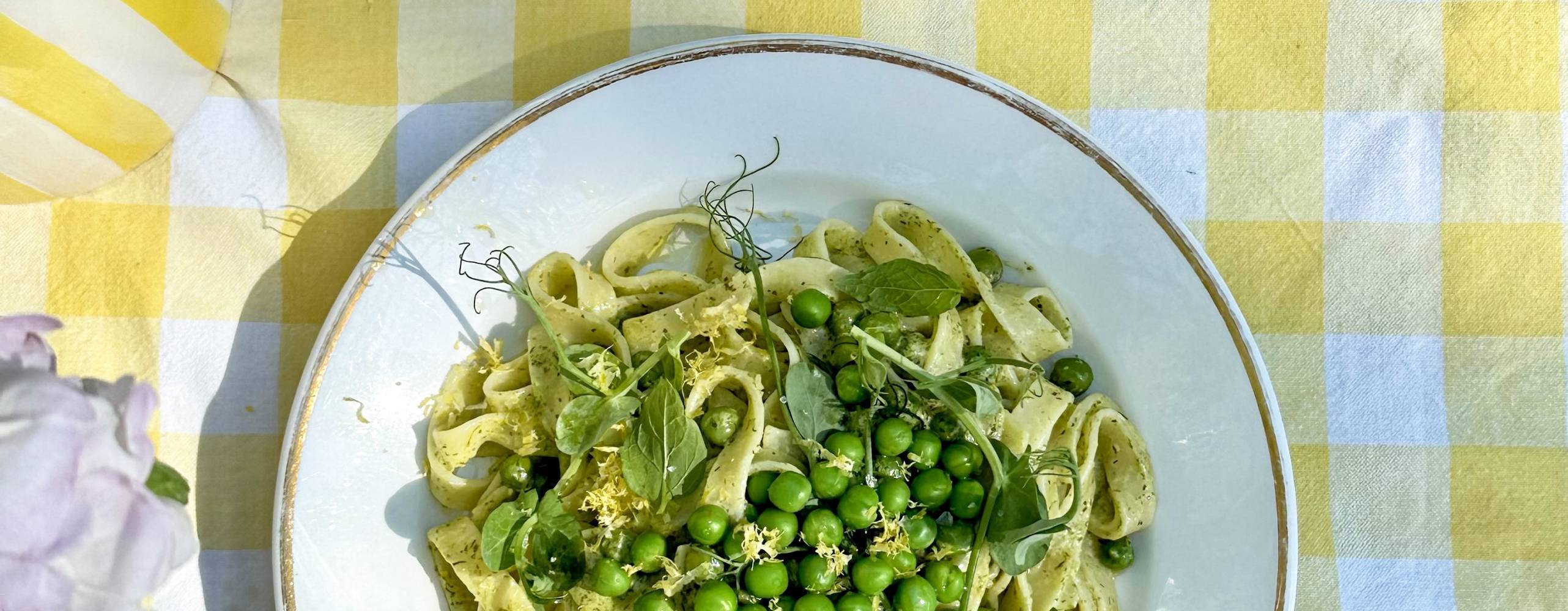 Tallrik med pasta och ärtor på en gulrutig duk