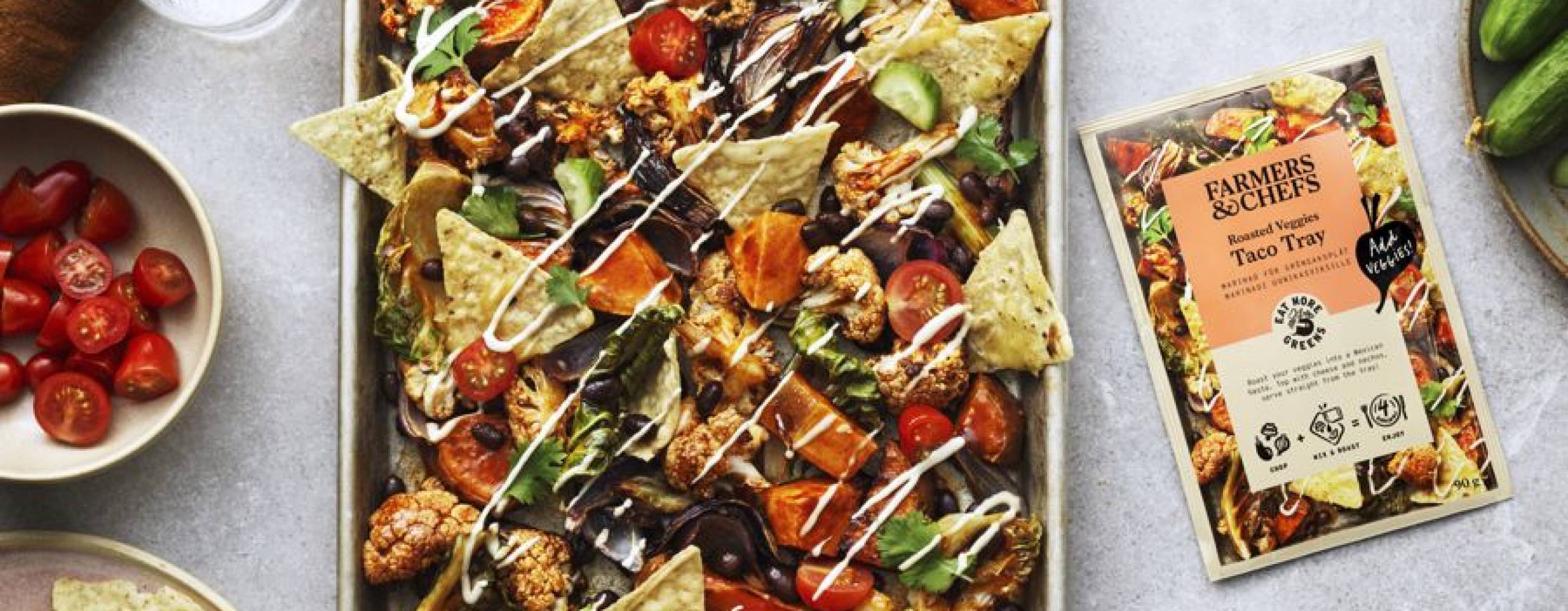 En plåt med dressade nachos på ett ljust bord med tillbehör på sidorna