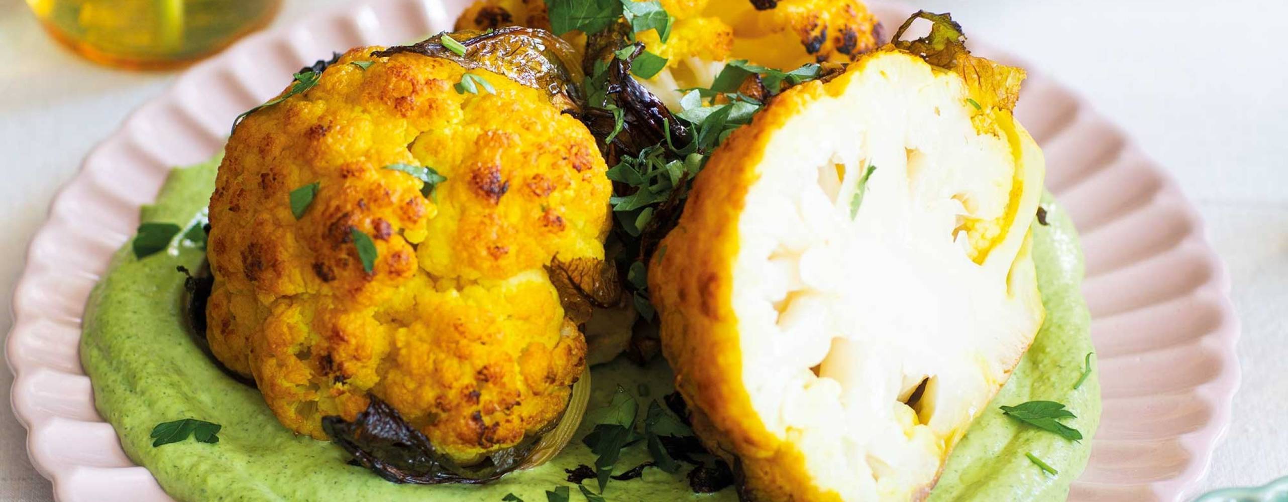 Rostad blomkål med grön tahinisås på en vit tallrik