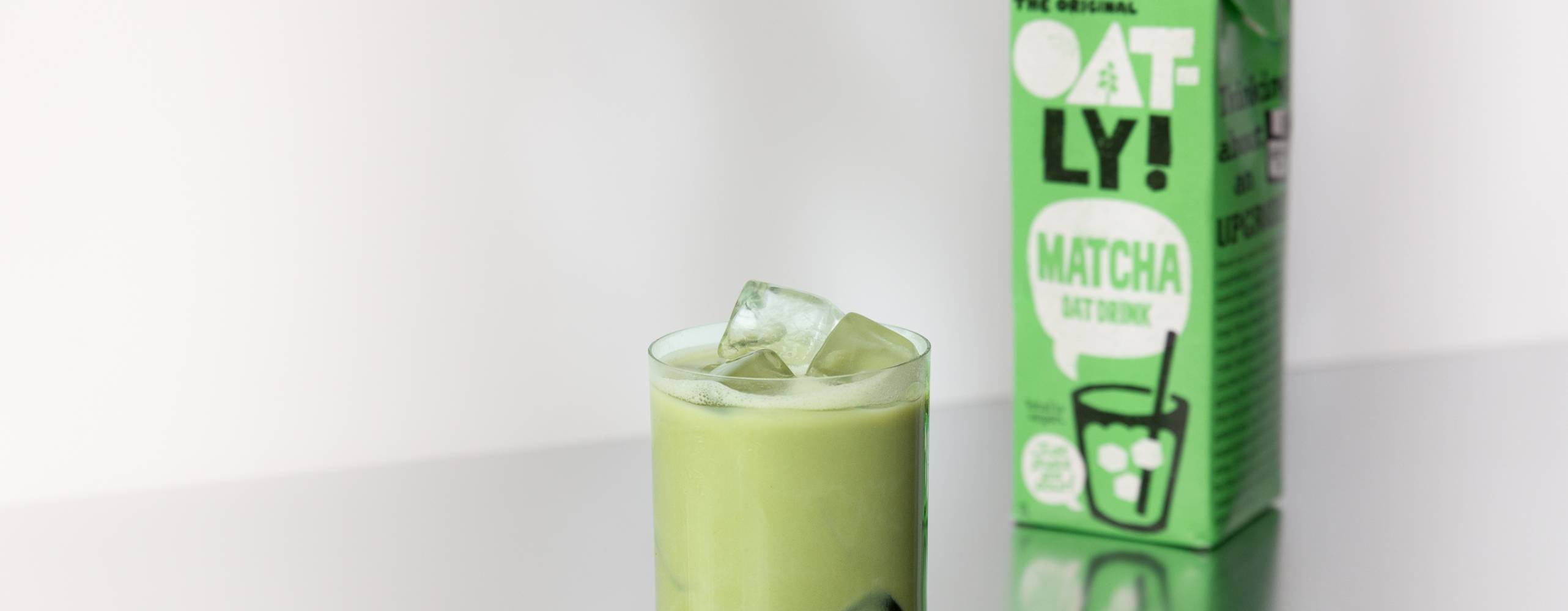 Ett glas med matcha latte och en tetra med färdigblandad matcha latte bredvid på ett silverbord.