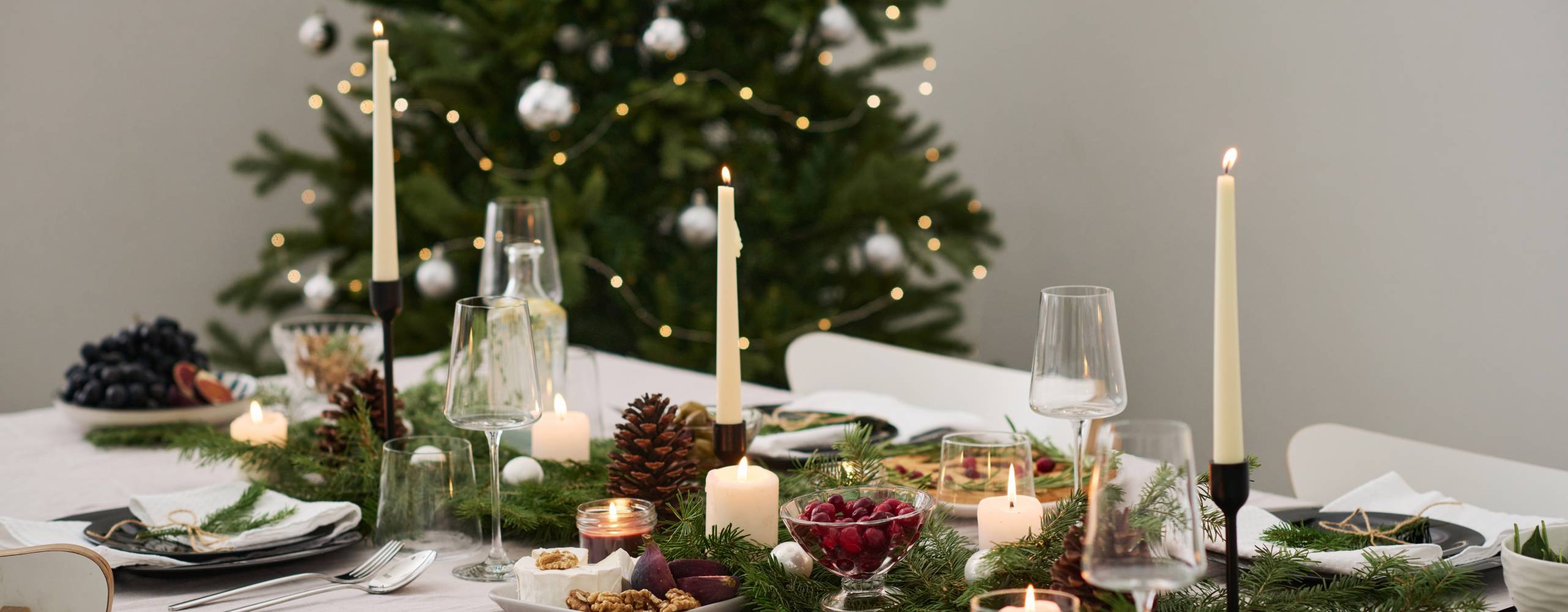 Ett uppdukat bord med julpynt och julgran i bakgrunden