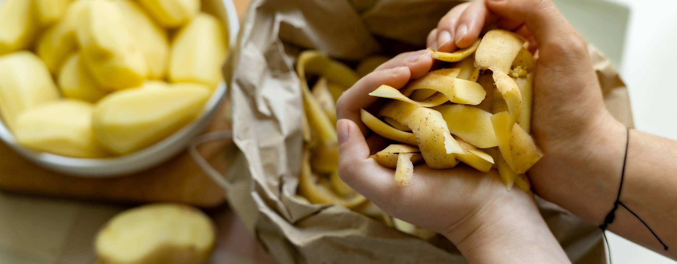 Kvinnliga händer kastar ekologiska potatisskinn i en papperspåse för vidare bearbetning av organiskt avfall. Sortering och återvinning av sopor.