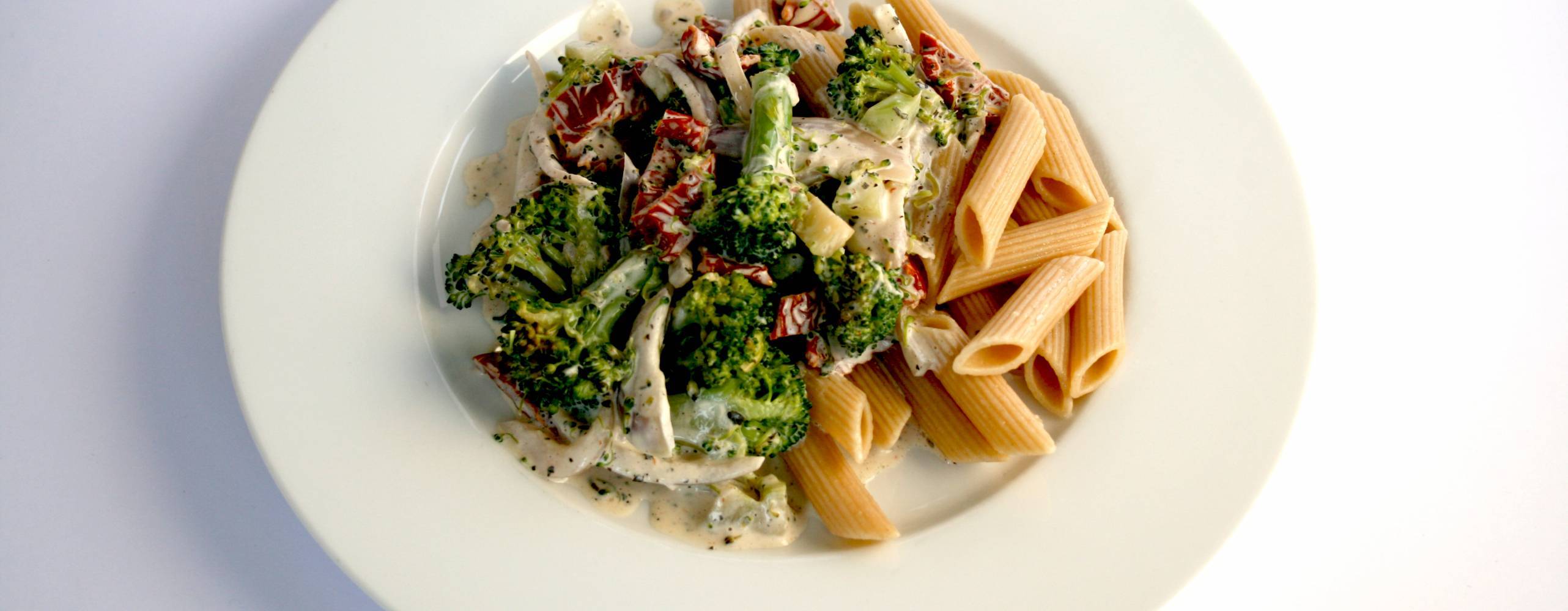 Pasta med broccoli och soltorkade tomater på en vit tallrik